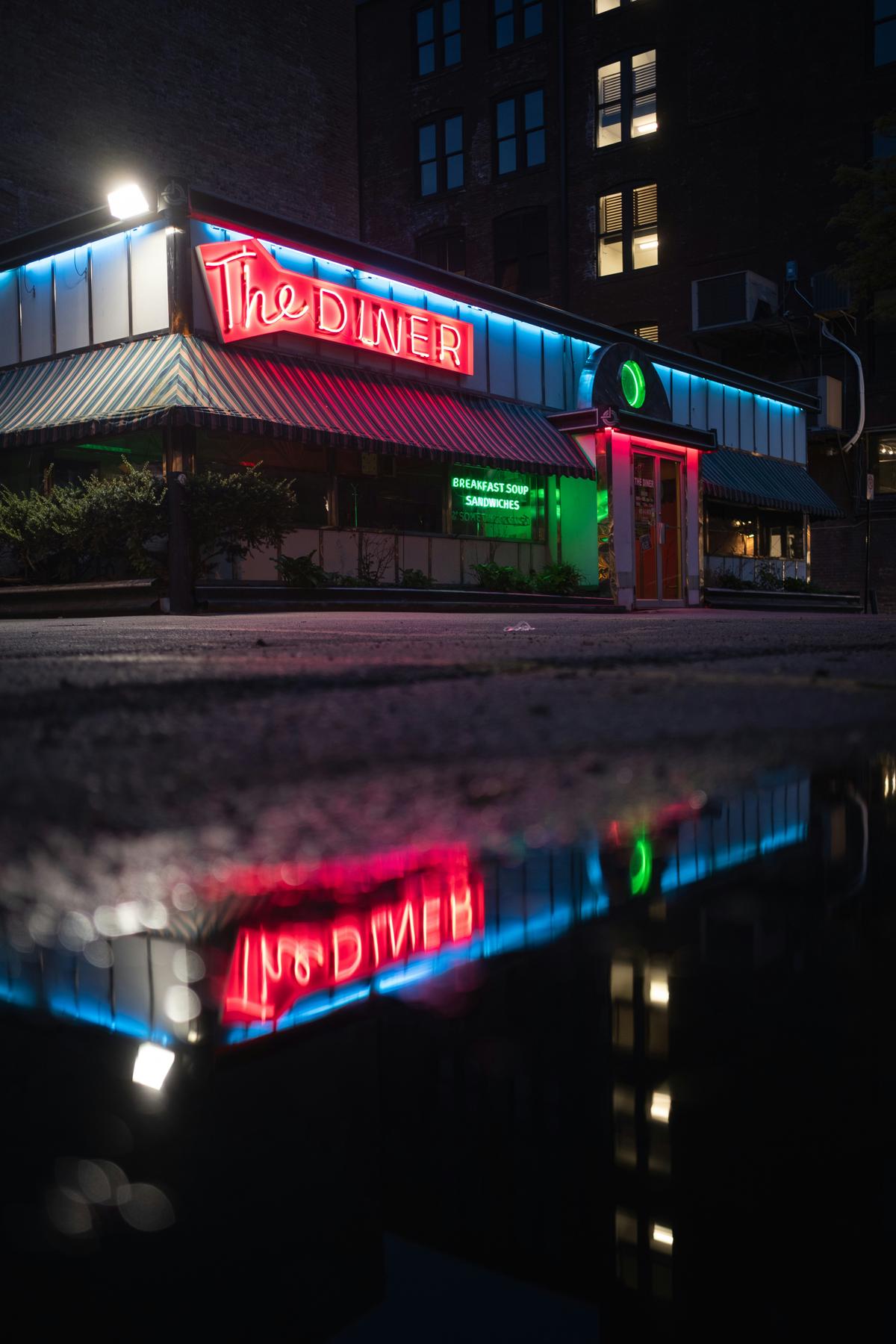 Exterior of a classic 1950s American diner with neon signs and parked vintage cars